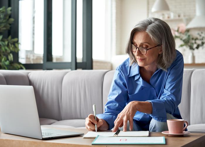Vrouw met blauwe blouse maakt notities en kijkt naar laptop