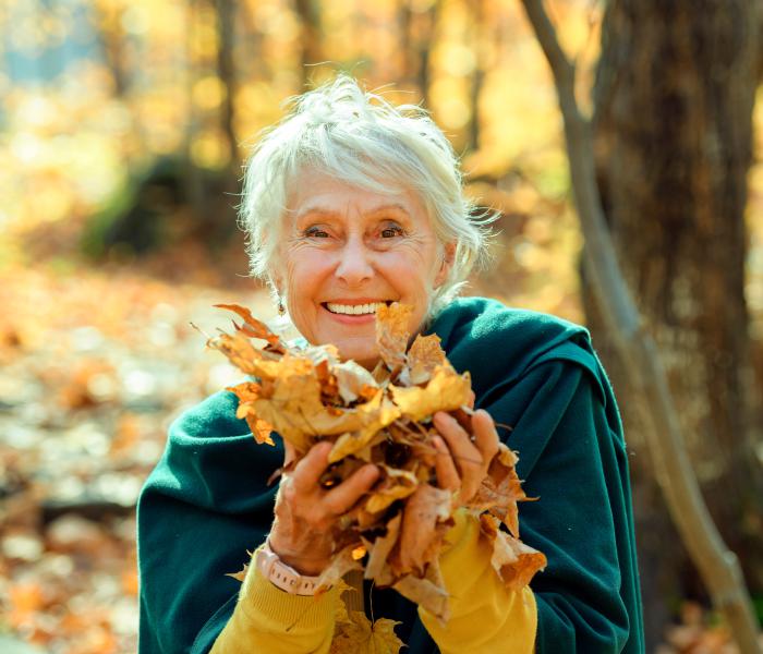 Blije oudere dame met herfstbladeren