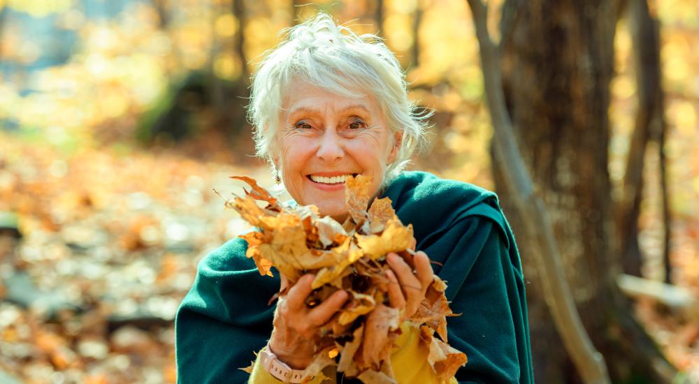 Blije oudere dame met herfstbladeren