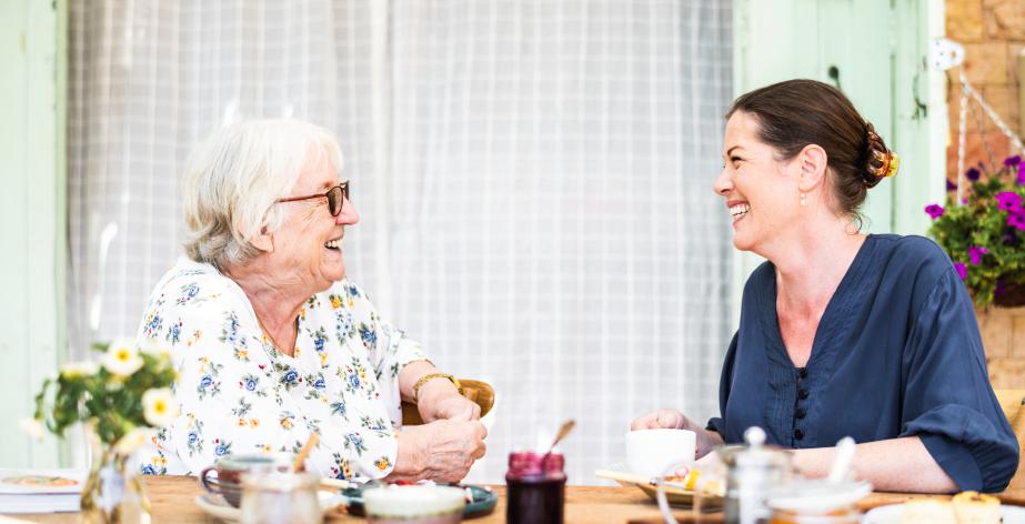 Oudere dame met haar thuishulp, lachend in gesprek